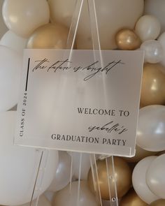 a welcome sign hanging from the side of a balloon wall with white and gold balloons