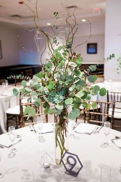 a vase filled with greenery sitting on top of a white table cloth covered table