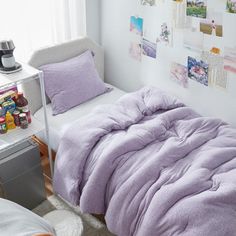 a bed with purple comforter and pillows next to a white desk in a bedroom