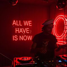 a dj in front of a neon sign that says all we have is now