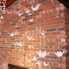 some paper birds are hanging on a brick wall near a fire place with a fireplace