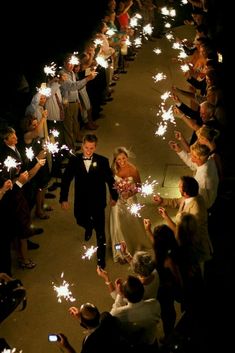 a bride and groom walking down the aisle with sparklers