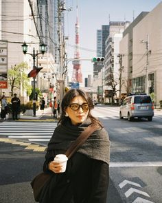 a woman standing on the side of a road holding a coffee cup