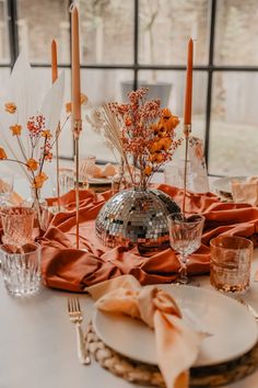 the table is set with orange napkins and silver vases, candles, and plates