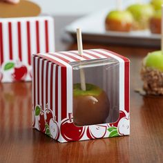 an apple in a box sitting on a table next to some apples with sticks sticking out of it