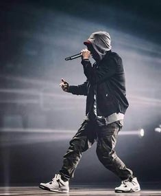 a male in a black jacket and white sneakers is holding a microphone while standing on stage