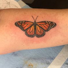 an orange and black butterfly tattoo on the right arm, with dots around it's wings