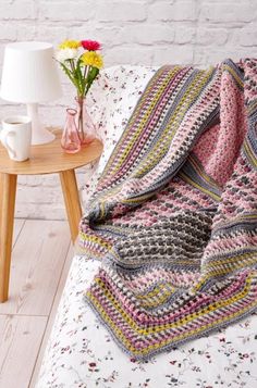 a crocheted blanket sitting on top of a bed next to a vase with flowers