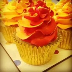 three cupcakes with red and yellow frosting on them sitting on a plate