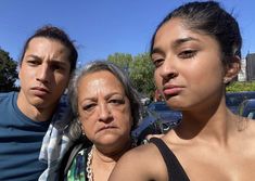 three people standing next to each other in front of a parking lot full of cars