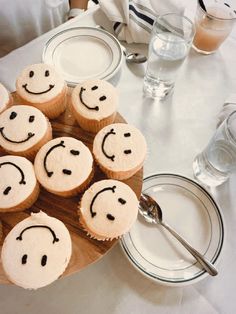 cupcakes with faces drawn on them sitting on a wooden platter at a table