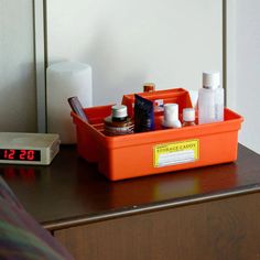 an orange container with various items on it sitting on a table next to a clock