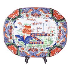 an orange and blue plate with floral designs on the border, sitting on a stand