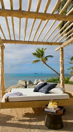 a bed sitting on top of a sandy beach under a wooden pergoline next to the ocean