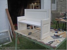 a white bench sitting on top of a wooden table next to a building and tools