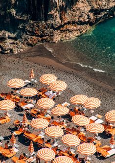 many orange and white umbrellas are set up on the sand near the water's edge