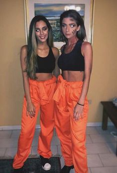 two women standing next to each other wearing orange pants and crop tops with black bras