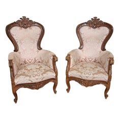 a pair of carved wood chairs with pink upholstered fabric on the back and arms