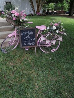 a pink bicycle with flowers in the basket is parked next to a chalkboard sign