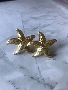 Vintage Goldtone Starfish Earrings  1 inch x 1 inch  Post earringsDisclaimer: All items in our store are vintage and pre-loved, which means they may show signs of gentle wear, including small dings, scratches, or other imperfections that add to their unique character. We do our best to describe and photograph each item accurately, but please feel free to reach out with any questions before purchasing. Thank you for appreciating the charm of vintage treasures! Vintage Gold Earrings For Beach, Summer Ocean-inspired Star Earrings, Gold Starfish Earrings, Ocean-inspired Gold Shell Earrings, Ocean-inspired Starfish Charm Dangle Earrings, Starfish Earrings, Starfish, Jewelry Earrings Studs, Post Earrings