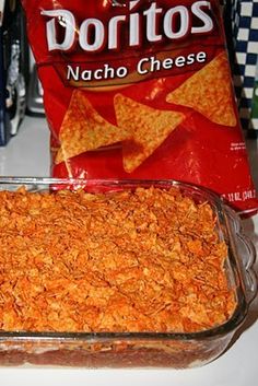 a glass dish filled with nacho cheese next to a bag of doritos