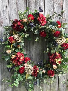 a wreath with red flowers and greenery hanging on a wooden fence, ready to be hung