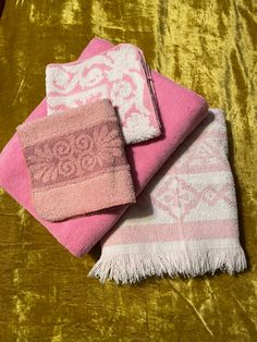 three towels are sitting on top of a gold velvet tablecloth with pink and white designs