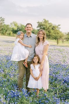 a man, woman and two children are standing in a field of bluebonnets