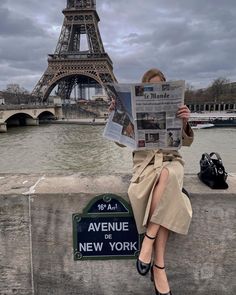 a woman sitting on a ledge reading a newspaper in front of the eiffel tower