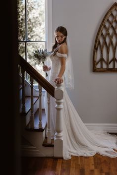 a woman in a wedding dress is standing on the stairs with her bouquet and looking at the camera