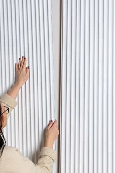 a woman holding onto the side of a white wall with vertical blinds on it's sides