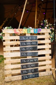 a wooden crate with chalk writing on it and flowers in the background at an outdoor event