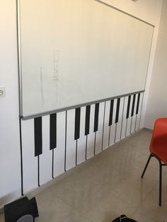 a white board with black and white piano keys on it next to a red chair