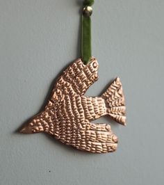 a metal fish ornament hanging on a wall with a green cord attached to it