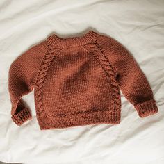 an orange knitted sweater laying on top of a white bed sheet with the bottom half turned down