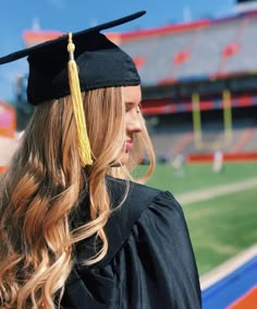 a woman in graduation gown and cap looking out at the football field from behind her