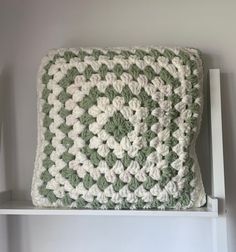 a green and white crocheted pillow sitting on top of a shelf