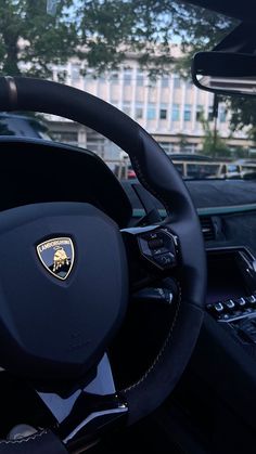 the steering wheel and dashboard of a car in front of a large building with trees