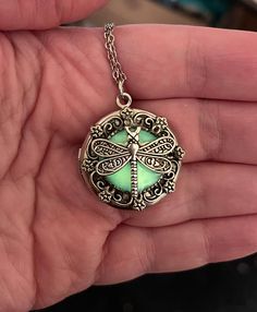 This enchanting locket possesses a secret that comes alive as the night approaches - it glows in the dark. A delicate silver dragonfly spreads its wings on top of a yellow orange background that glows a bright green in the dark. The bezel it sits on has a floral detail that brings out the nature theme of this piece.  It hangs from an adjustable silver toned chain, and can be worn from 18 inches to 20 inches.  The locket (about 1 inch in diameter) opens up to stash your special photos/treasures i Mystical Luminous Jewelry Gift, Mystical Luminous Jewelry For Gifts, Green Locket Jewelry For Gift, Luminous Spiritual Jewelry For Gifts, Luminous Spiritual Jewelry As A Gift, Spiritual Luminous Jewelry As Gift, Green Luminous Round Jewelry, Luminous Pendant Jewelry Gift, Luminous Pendant Jewelry For Gifts