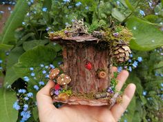 a hand holding up a small fairy house made out of tree stumps and mushrooms