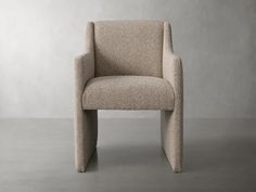 a beige chair sitting on top of a floor next to a gray wall with no one in it