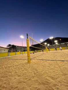 an empty volleyball court at night with lights on the side and people playing volleyball in the sand