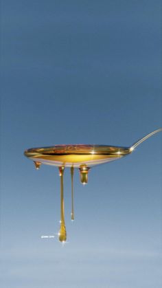 a spoon with liquid dripping from it is in the air and on top of a plate