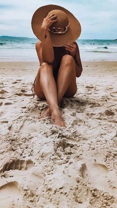 a woman is sitting on the beach wearing a hat