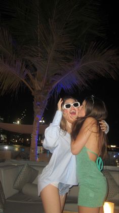 two beautiful young women standing next to each other in front of a palm tree at night