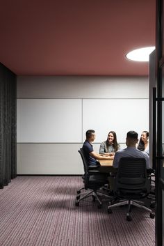 three people sitting at a table in an office setting with pink walls and carpeting