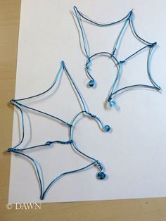 three wire wrapped spider webs sitting on top of a piece of paper with blue beads