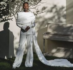 a man in white clothes standing next to a tree and bench with his hands on his hips