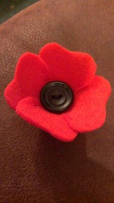 a red felt flower with a black button on it's center sits atop a brown surface