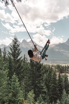 a man is swinging from a rope in the air with trees and mountains behind him